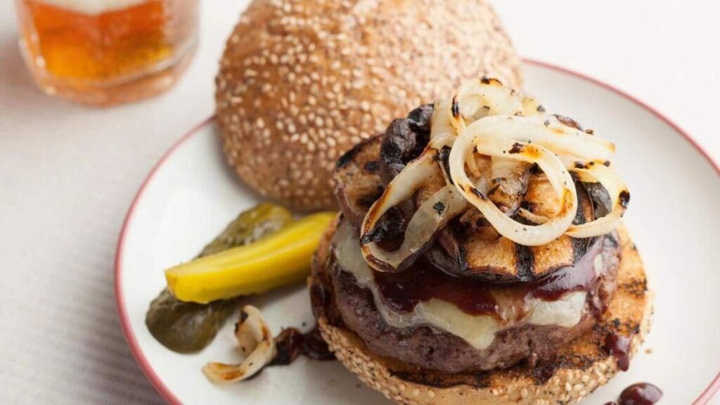 A hamburger with onions and pickles on the side.