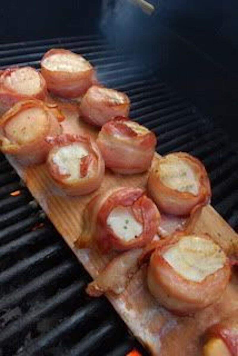 A wooden board with bacon wrapped scallops on it.
