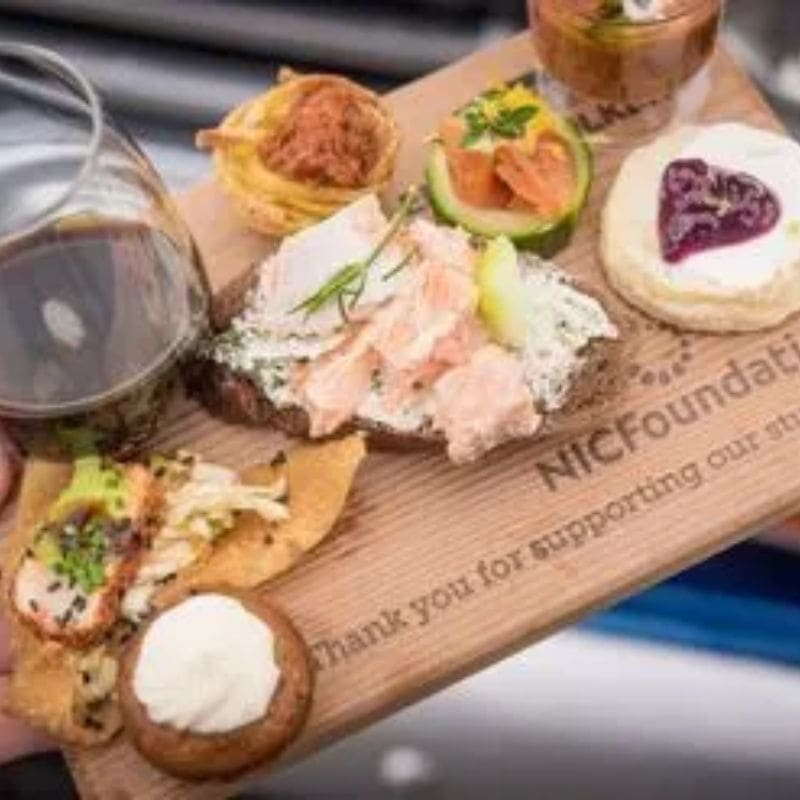 A wooden board with food on it and a glass of wine.